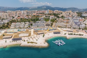 Vista aérea de una ciudad costera con playa, edificios y montañas al fondo.