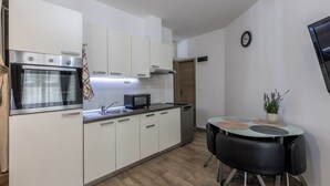 A compact kitchen with white cabinets, a built-in oven, a microwave, a sink, and a small dining table with chairs. - Rećina, Studio apartment near Žnjan Beach (Split)