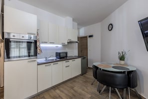 A compact kitchen with white cabinets, a built-in oven, a microwave, a sink, and a small dining table with chairs. - Rećina, Studio apartment near Žnjan Beach (Split)