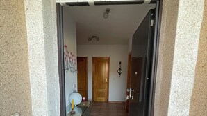 Un corridoio con pavimento piastrellato, una porta in vetro e una porta in legno alla fine.