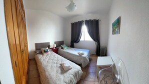 Una stanza con due letti, una scrivania, una sedia, un termosifone e una finestra con tende.