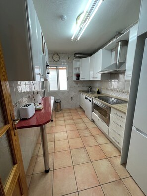 A kitchen with white cabinets, a red countertop, a stainless steel oven, and a tiled floor.