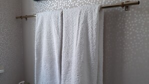 Een badkamer met een handdoekhouder met twee handdoeken, een plank met toiletartikelen en ingelijste foto's aan de muur.
