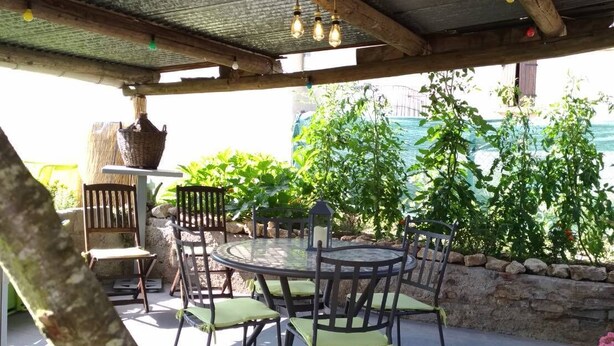 Een terras buiten met een ronde tafel en stoelen, een hangmand en een stenen muur.