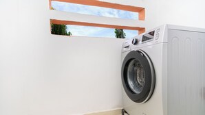 A front-loading washing machine in a corner of a room with a white wall and a small window. - Luxury apartment complex with a pool and gym, 10 minutes from Guéliz (marrakech)