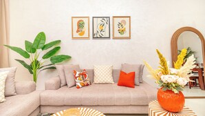 A living room with a sofa, a large plant, a vase with flowers, and framed artwork on the wall. - Luxury apartment complex with a pool and gym, 10 minutes from Guéliz (marrakech)