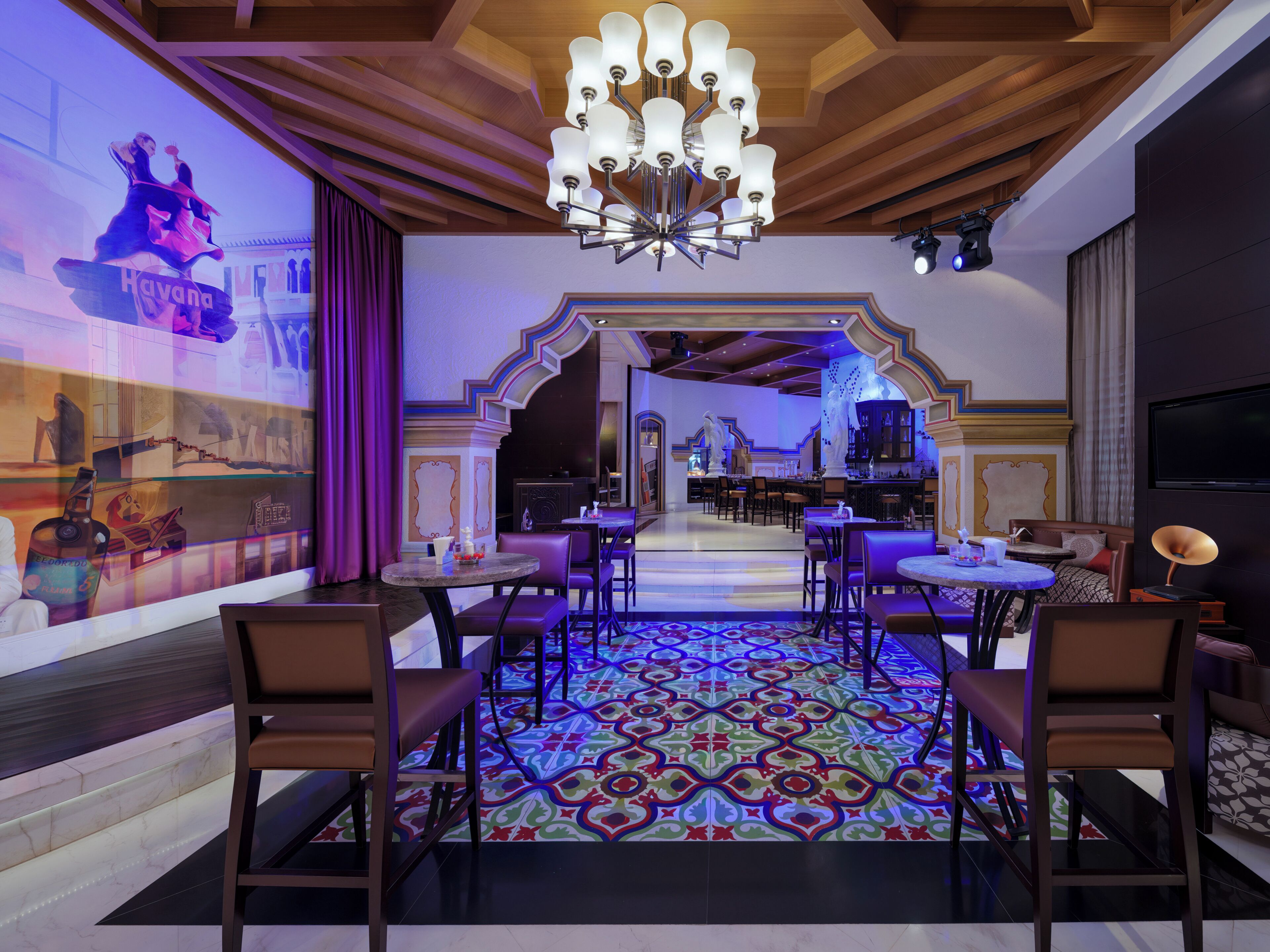 Un hall de hotel con zona de bar, asientos y una pantalla grande mostrando una escena.