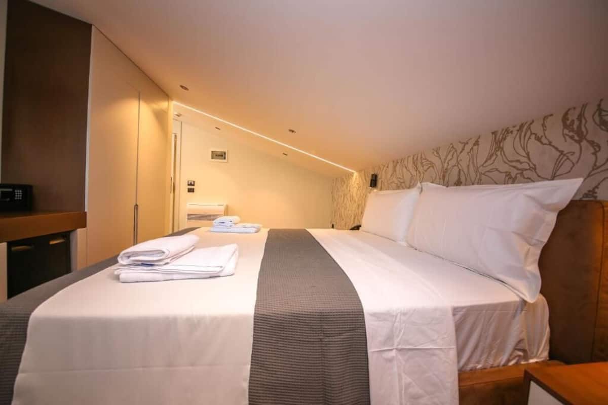 A hotel room with a neatly made bed, a bedside table, a wall-mounted TV, and a door leading to a bathroom.