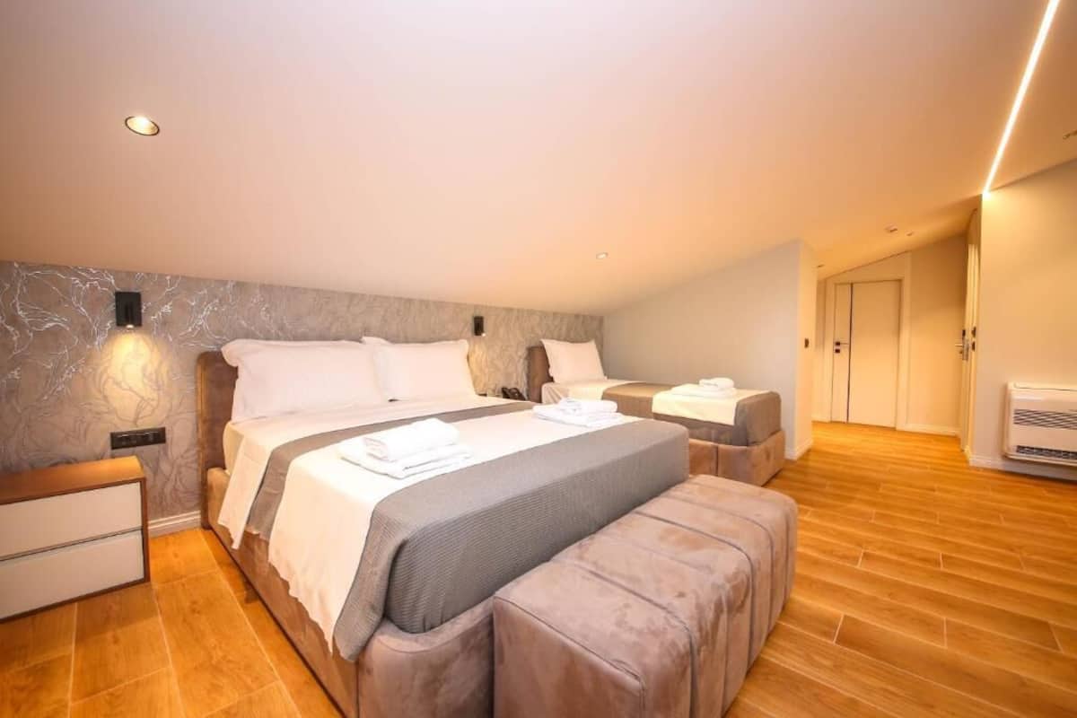 A modern hotel room with a large bed, a bedside table, a bench, and a wardrobe.