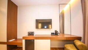 Una habitación moderna con un escritorio de madera, una cafetera integrada, un televisor y un sofá.