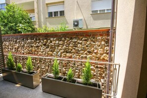 Un muro de piedra con barandilla de metal, plantas en macetas y un edificio al fondo.