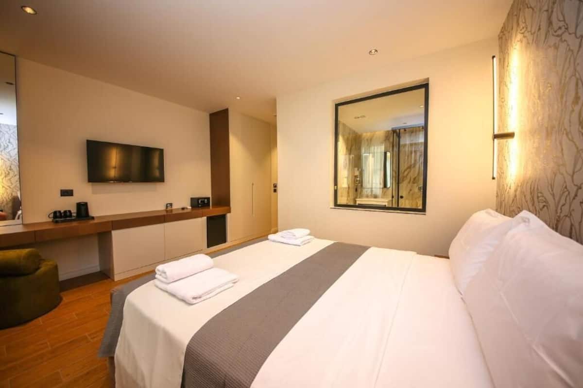A hotel room with a bed, a TV, a mirror, and a desk with a chair.
