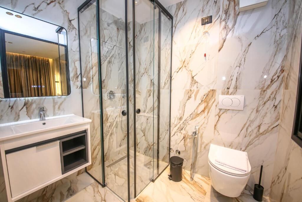Un baño moderno con ducha de vidrio, lavamanos blanco y retrete.