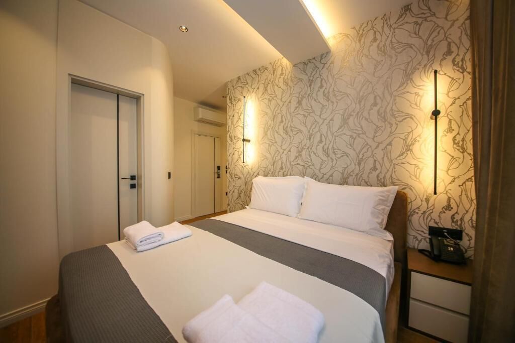 Quarto de hotel com cama, mesas de cabeceira, guarda-roupa e papel de parede estampado.
