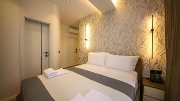 Quarto de hotel com cama, mesas de cabeceira, guarda-roupa e papel de parede estampado.