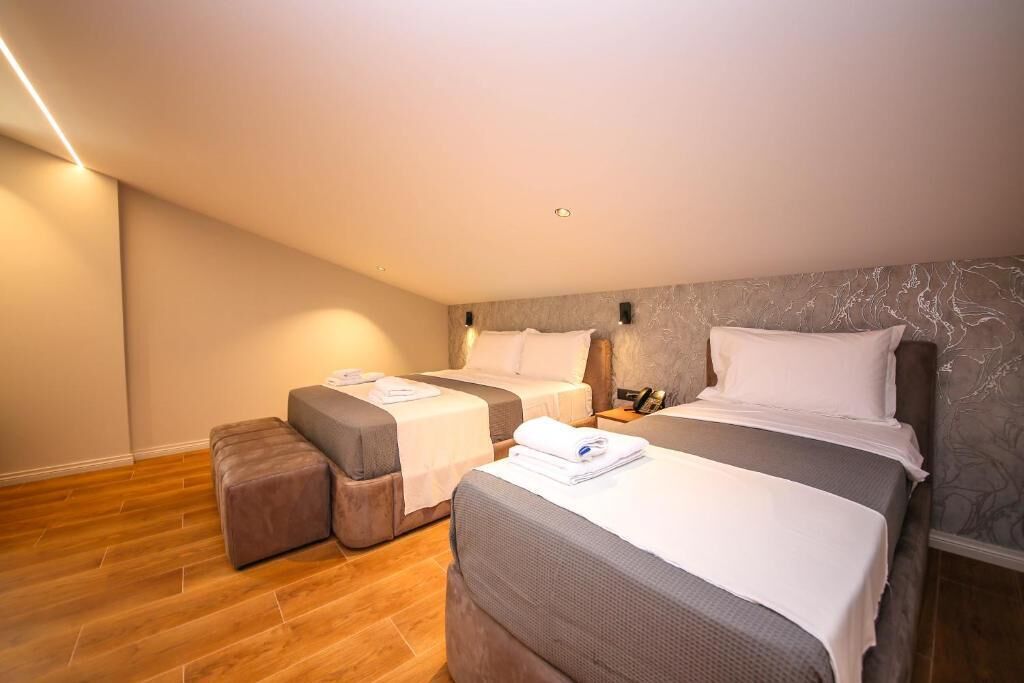 Quarto de hotel com duas camas, um pequeno espaço de estar e parede com padrão marmorizado.