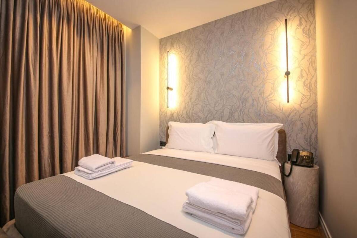 A hotel room with a large bed, two bedside tables, a telephone, and a wall-mounted light fixture.