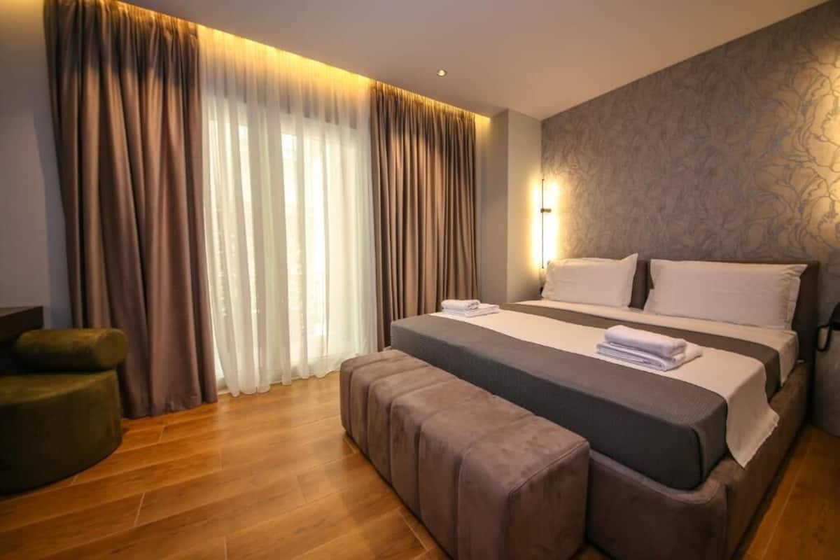 A hotel room with a large bed, a bench, a chair, and a wall-mounted light.