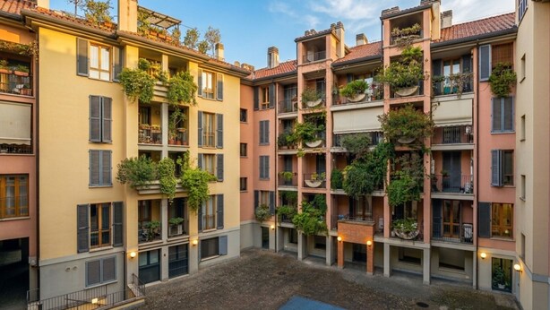 Un patio con edificios de varios pisos, balcones con plantas y una piscina pequeña.