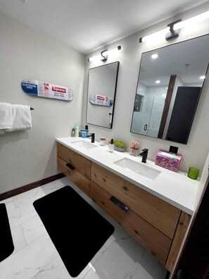 A bathroom with two sinks, wooden cabinets, a black rug, and a mirror with a 'Supreme' advertisement. - Luxury Blue Ridge Treehouse Retreat with Private Creek Fire Pit in Brevard, NC (Brevard)