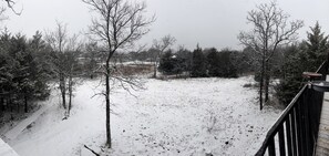 A snowy landscape with bare trees and a wooden deck.