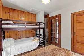 Een slaapkamer met stapelbed, houten wanden, een raam met gordijnen en een deur.
