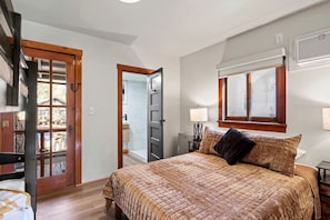 Ein Schlafzimmer mit einem Bett, einem Fenster, einer Tür und einem kleinen Tisch mit einer Lampe.