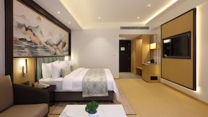 Een moderne hotelkamer met een bed, nachtkastje, lamp, televisie en kunst aan de muur.