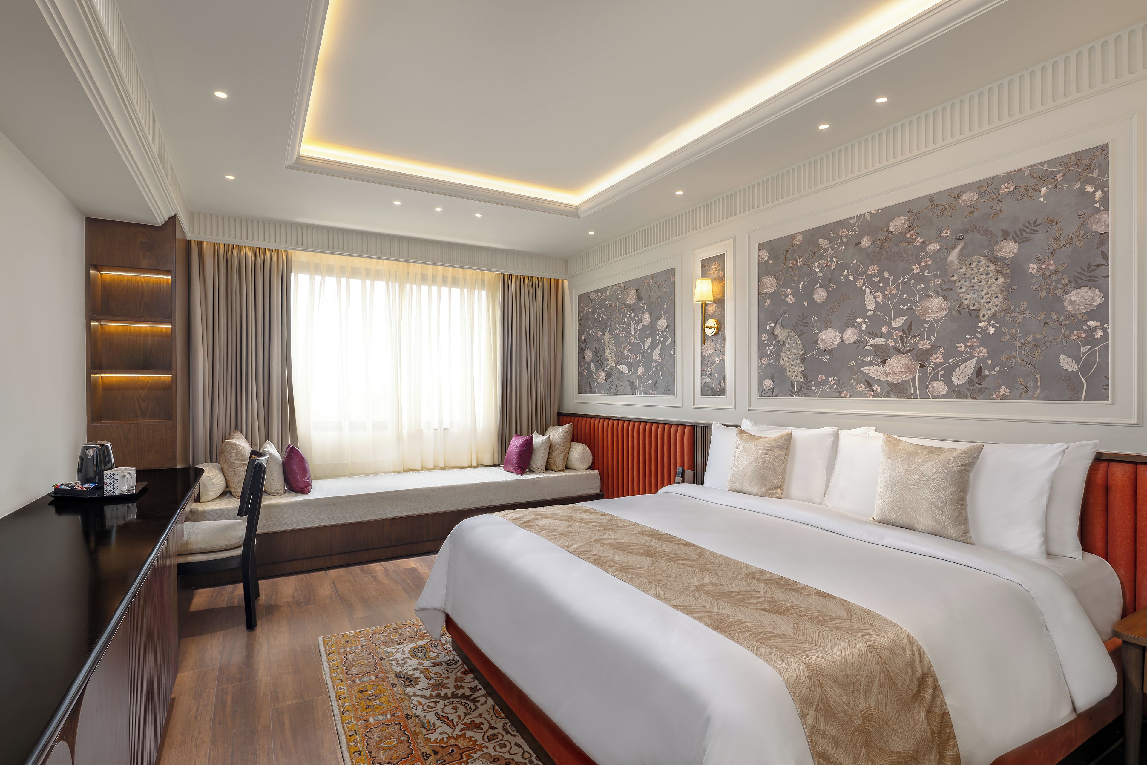A hotel room with a large bed, a bedside table, a window with curtains, a wall-mounted lamp, and a decorative wall panel.