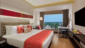 Hotelkamer met een groot bed, een bureau, een stoel, een televisie en uitzicht over de stad.
