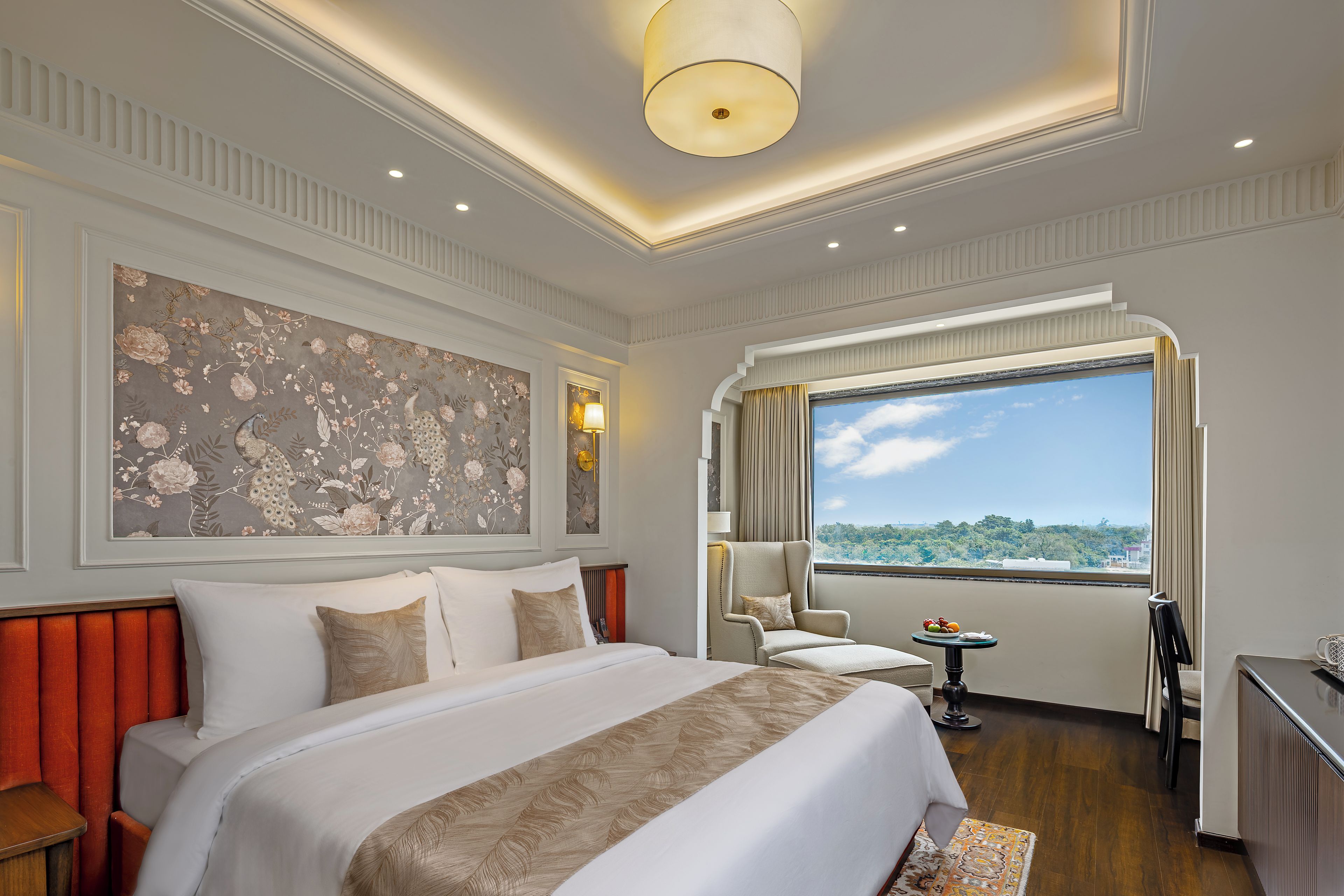 Une chambre d’hôtel avec un grand lit, une chaise, une petite table et une fenêtre donnant sur un beau paysage.