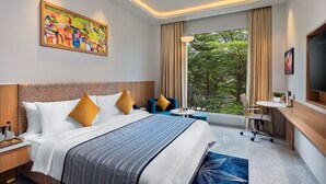 Een moderne hotelkamer met een groot bed, een bureau, een stoel, een televisie en een raam met uitzicht op bomen.
