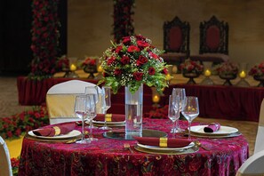A table set for a formal event with a red floral centerpiece, clear glassware, and a richly patterned tablecloth. - Fortune Select Lucknow  (Lucknow)