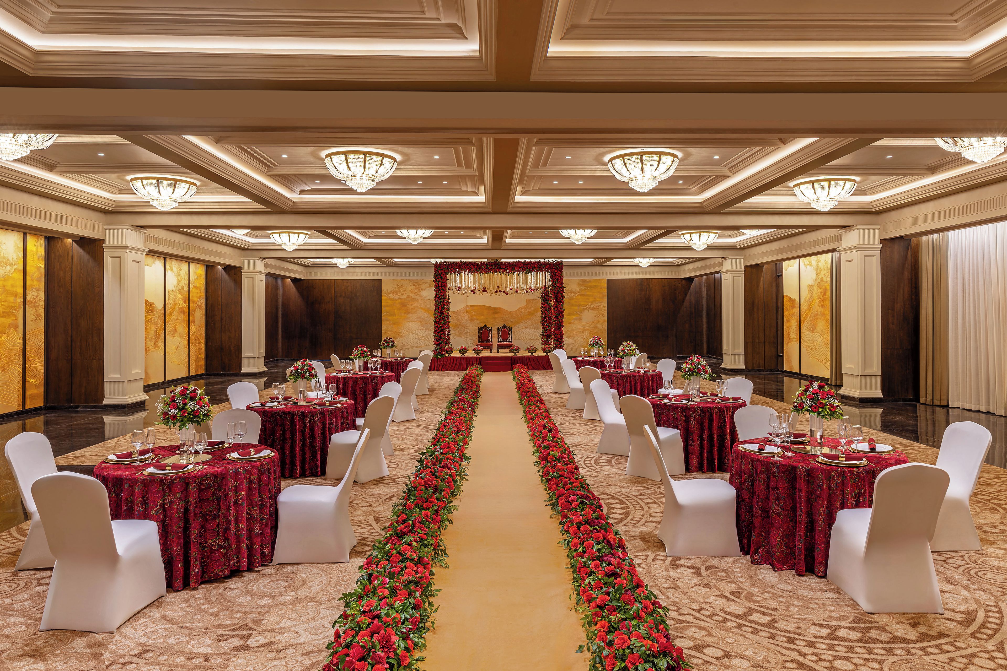 A banquet hall with tables set for a formal event, featuring a central aisle with floral decorations.