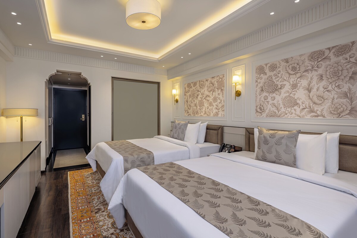 A hotel room with two beds, a desk, a door, and a patterned wallpaper.