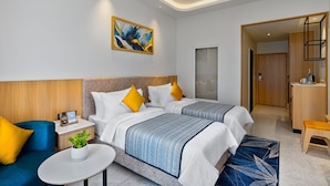 Een hotelkamer met twee bedden, een kleine tafel, een bank, een bureau en een badkamer zichtbaar door een open deur.