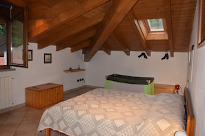 A bedroom with a sloped ceiling, a bed, a wooden bench, a shelf with a vase, and a window.