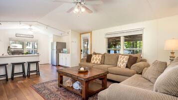 A spacious living area with a kitchen, a dining area with stools, a sofa set, a coffee table, and a ceiling fan.