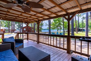 Une terrasse couverte avec des meubles en osier, une vue sur un lac et un chalet en arrière-plan.