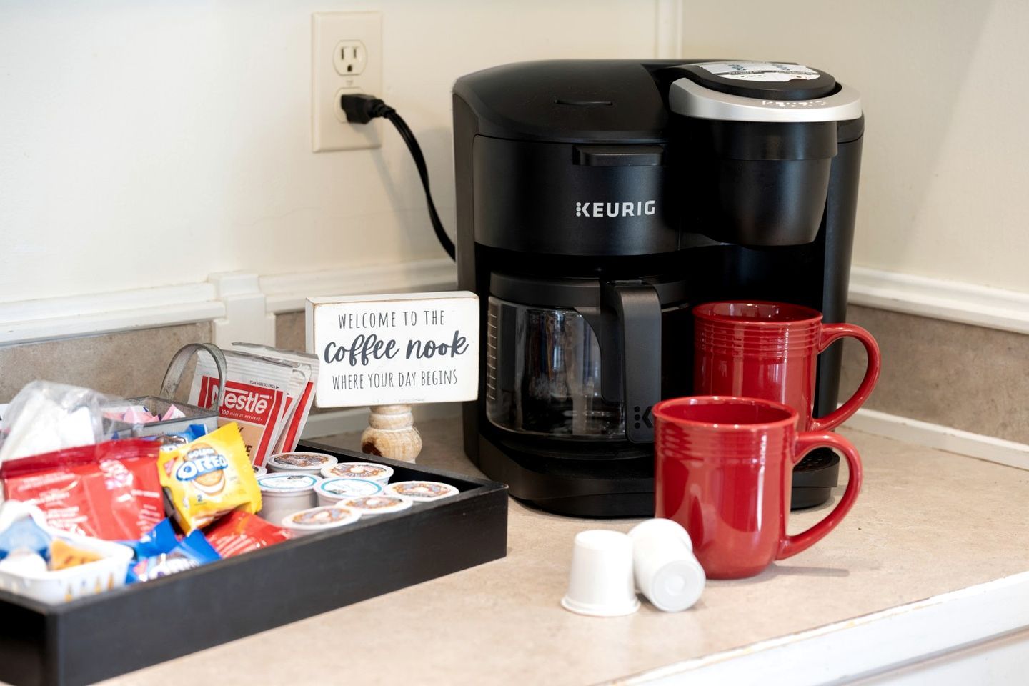 Eine Kaffeestation mit einer Keurig-Kaffeemaschine, roten Tassen und Kaffeekapseln auf einer Arbeitsplatte.