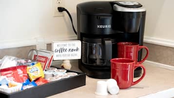 Eine Kaffeestation mit einer Keurig-Kaffeemaschine, roten Tassen und Kaffeekapseln auf einer Arbeitsplatte.