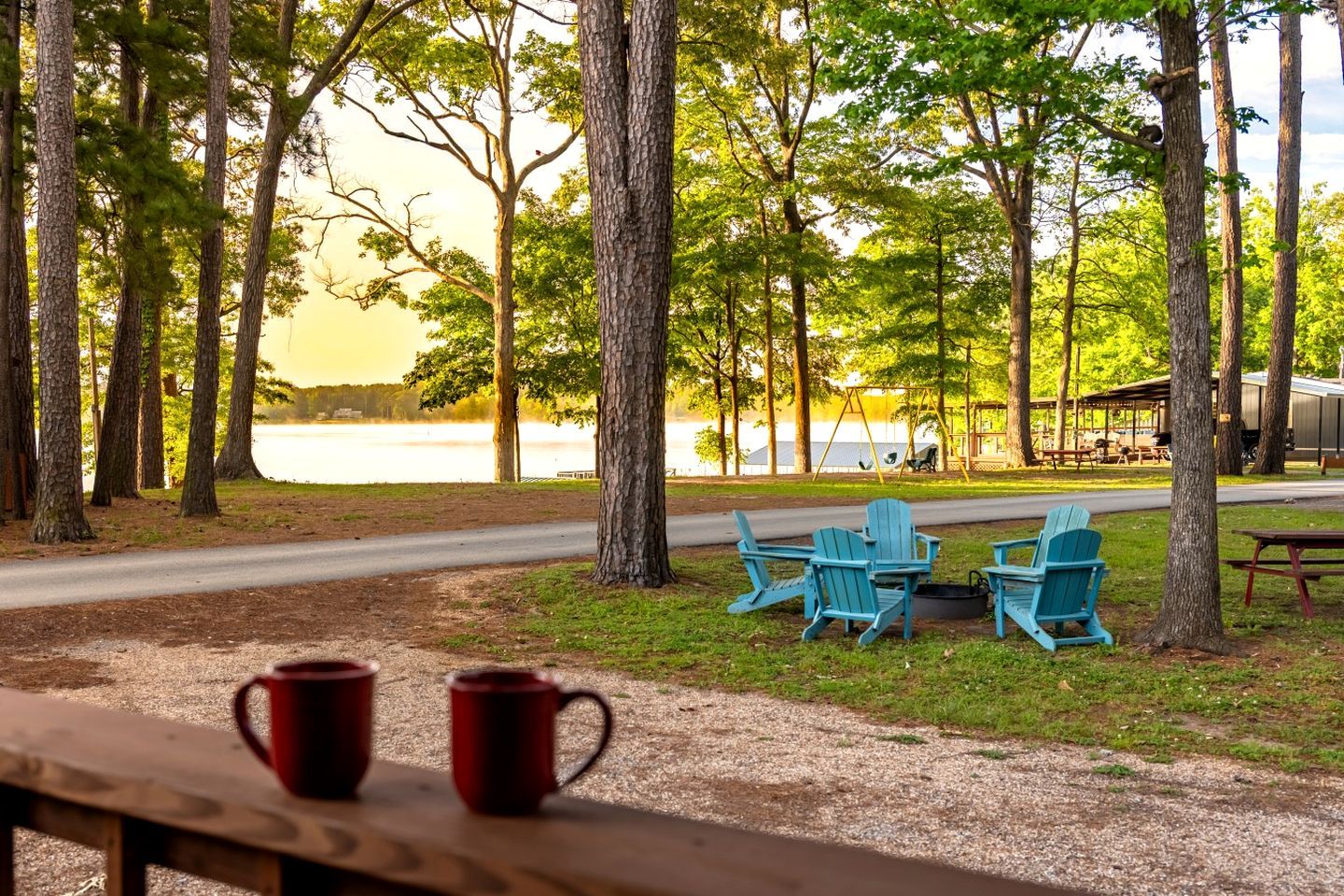 Un parque junto al lago con mesas de picnic, sillas Adirondack y un columpio.