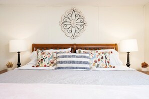 Un letto rifatto con cuscini a fiori e a righe, un elemento decorativo a parete e due lampade da comodino.