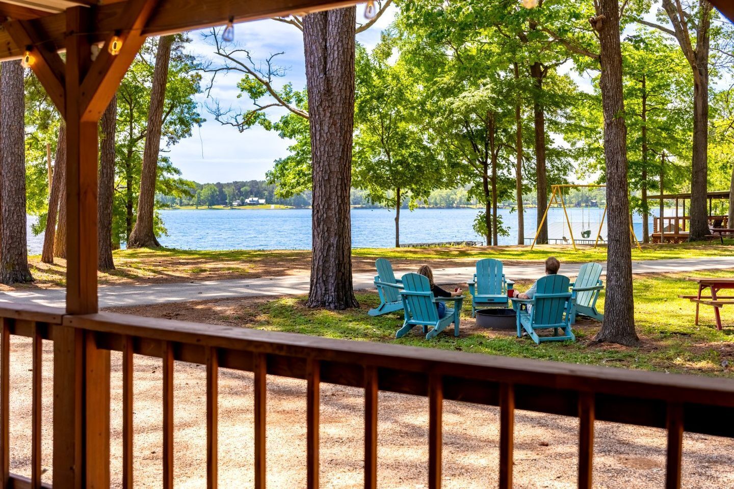 A lakeside view with a gazebo, chairs, and a swing set.
