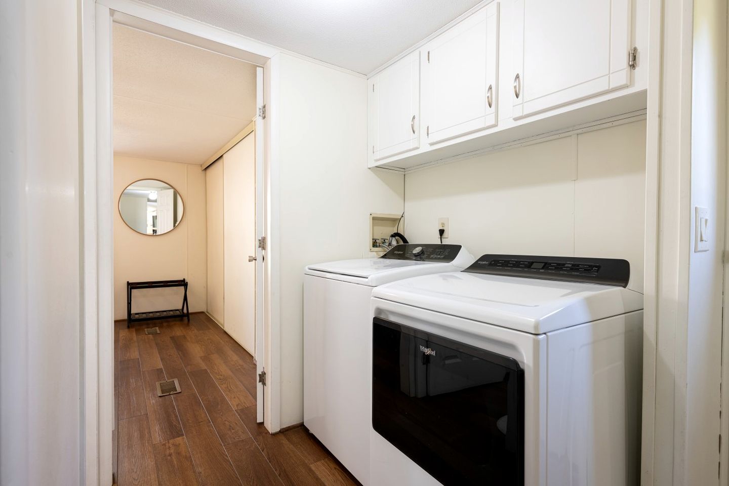 A laundry room with a washer and dryer, wooden flooring, and white cabinetry.
