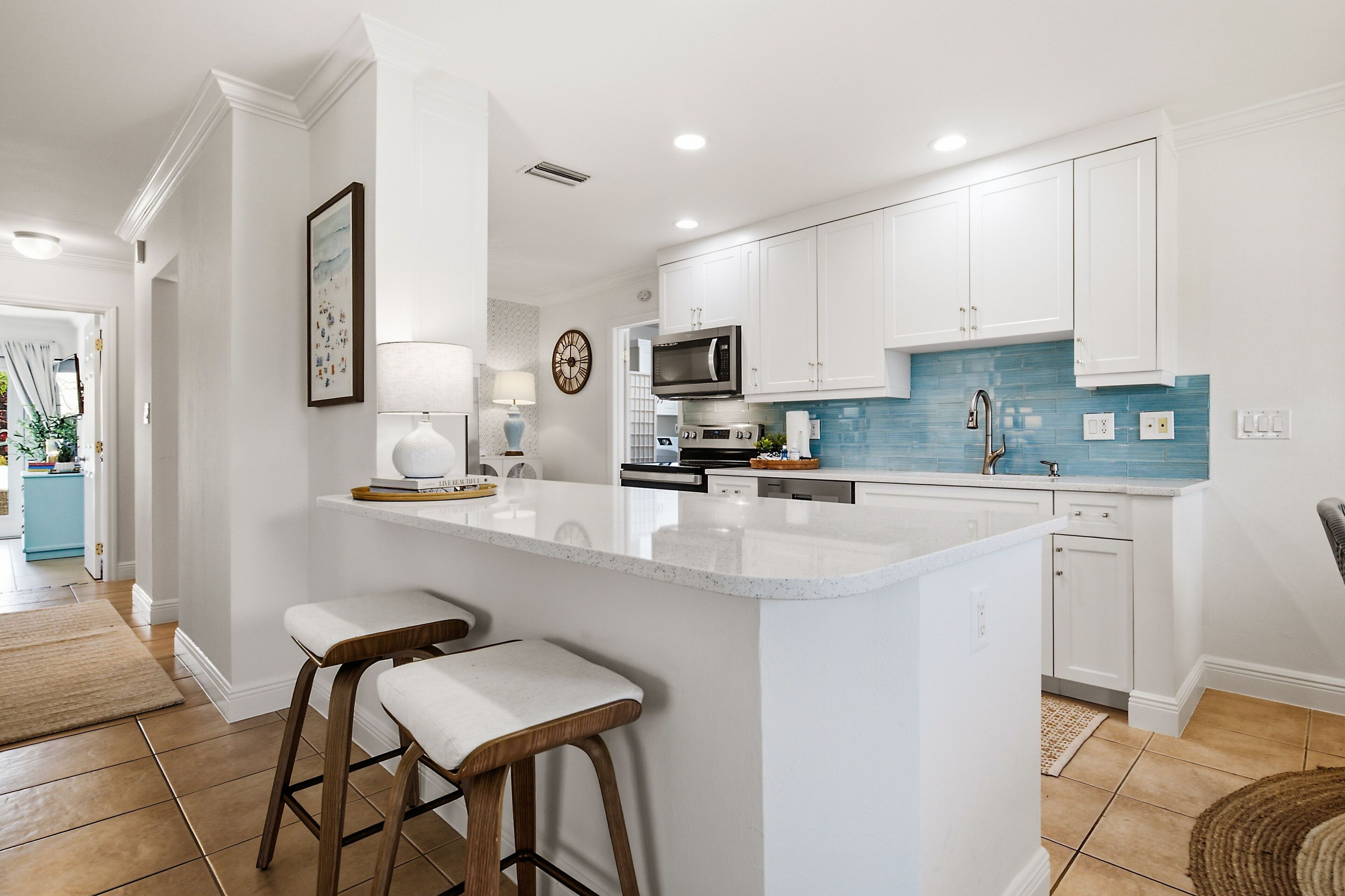 A modern kitchen with white cabinets, a blue backsplash, and a central island with bar stools.