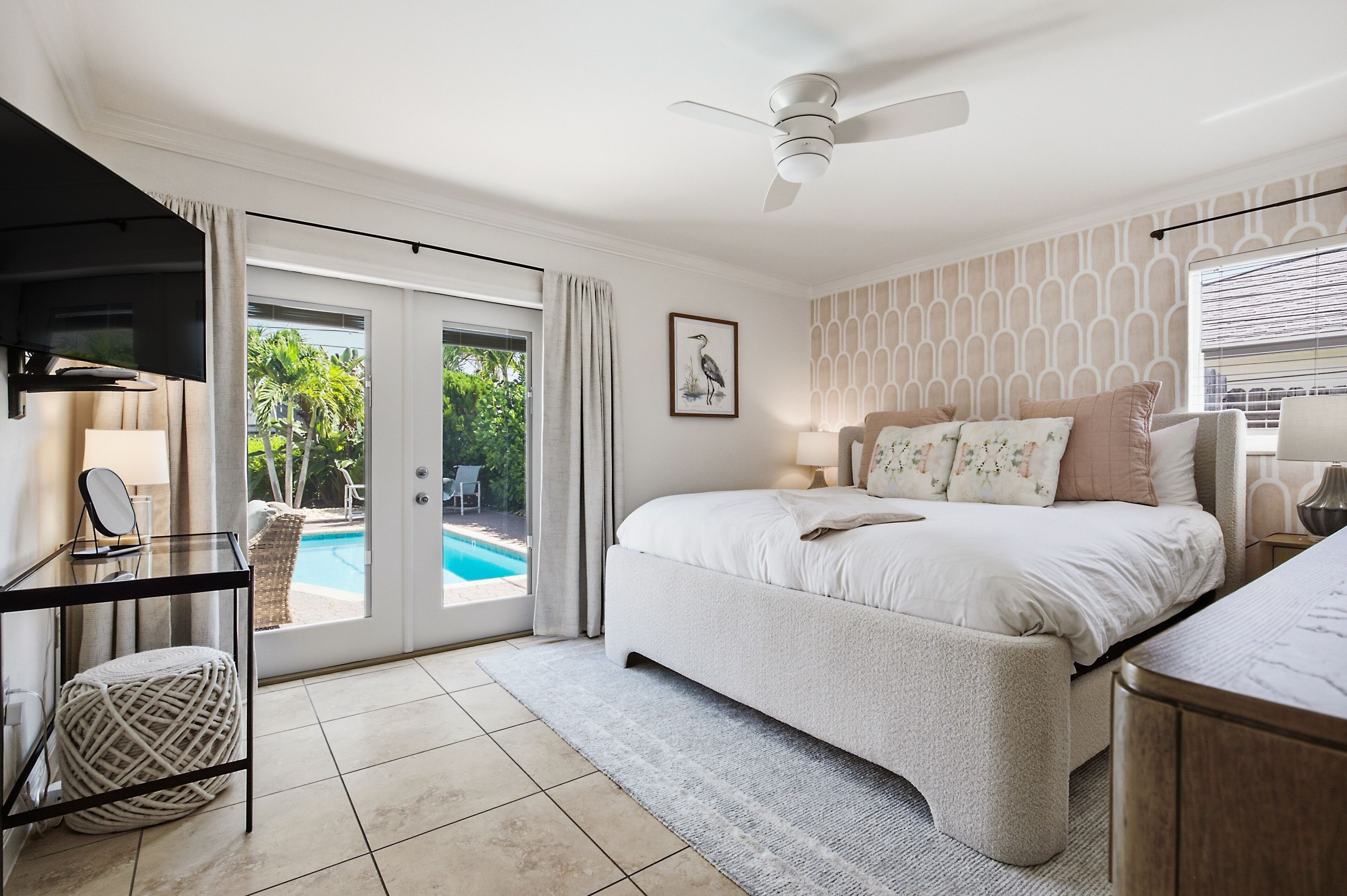 A bedroom with a bed, a ceiling fan, a TV, and a view of a swimming pool.
