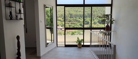 A spacious room with a large window, a balcony, and a view of a forested area.