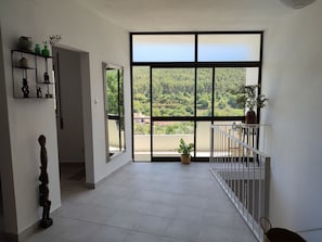 Ein geräumiges Zimmer mit großem Fenster, einem Balkon und Blick auf eine bewaldete Landschaft.
