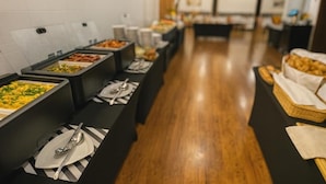 A buffet setup with various food items in black trays, a wooden floor, and a white tiled wall. - Hotel Bratislava (Bratislava)